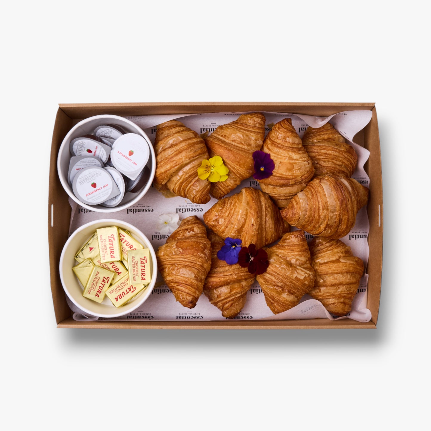 Box of croissants with small bowls of butter and jam on a white background