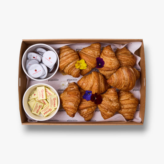 Box of croissants with small bowls of butter and jam on a white background